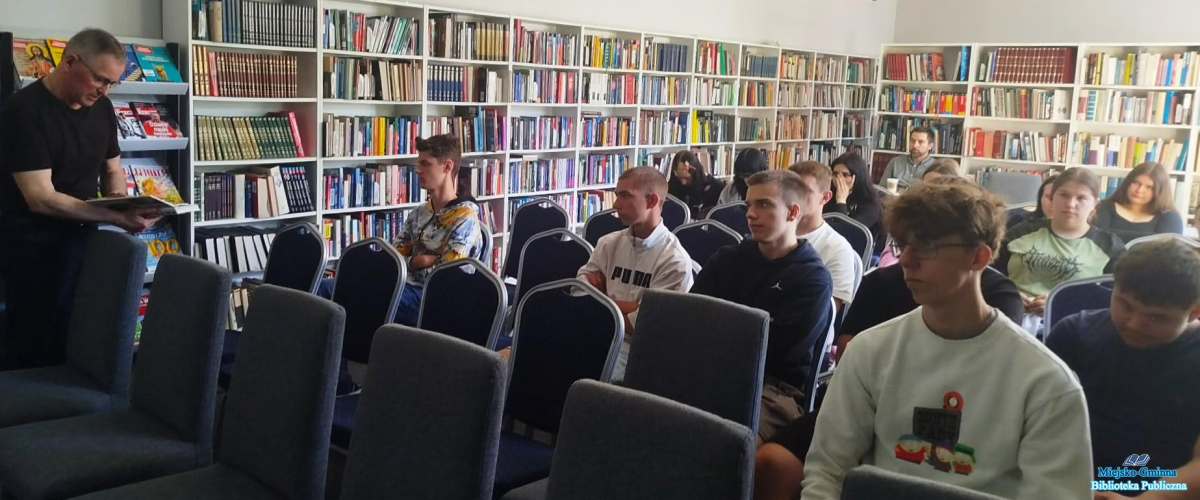 Młodzież siedzi, a Pan stoi obok i trzyma książkę
