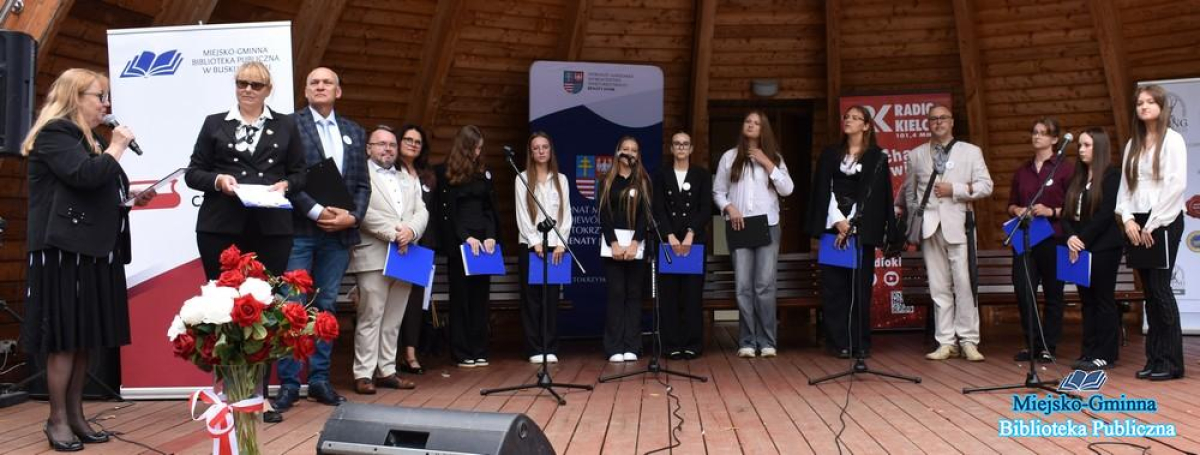 Pani stoi na scenie i mówi do mikrofonu do zebranych lektorów