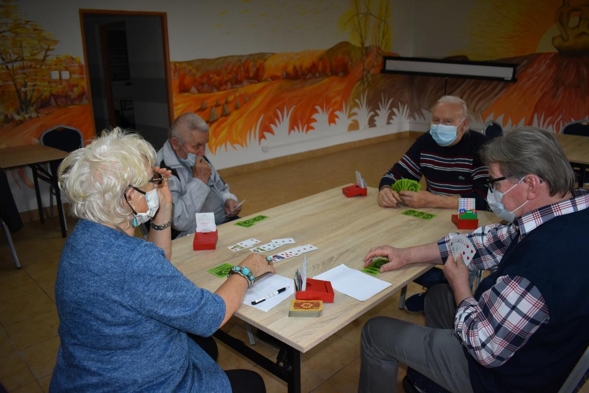 Cztery osoby siedzą przy stoliku i grają w brydża 