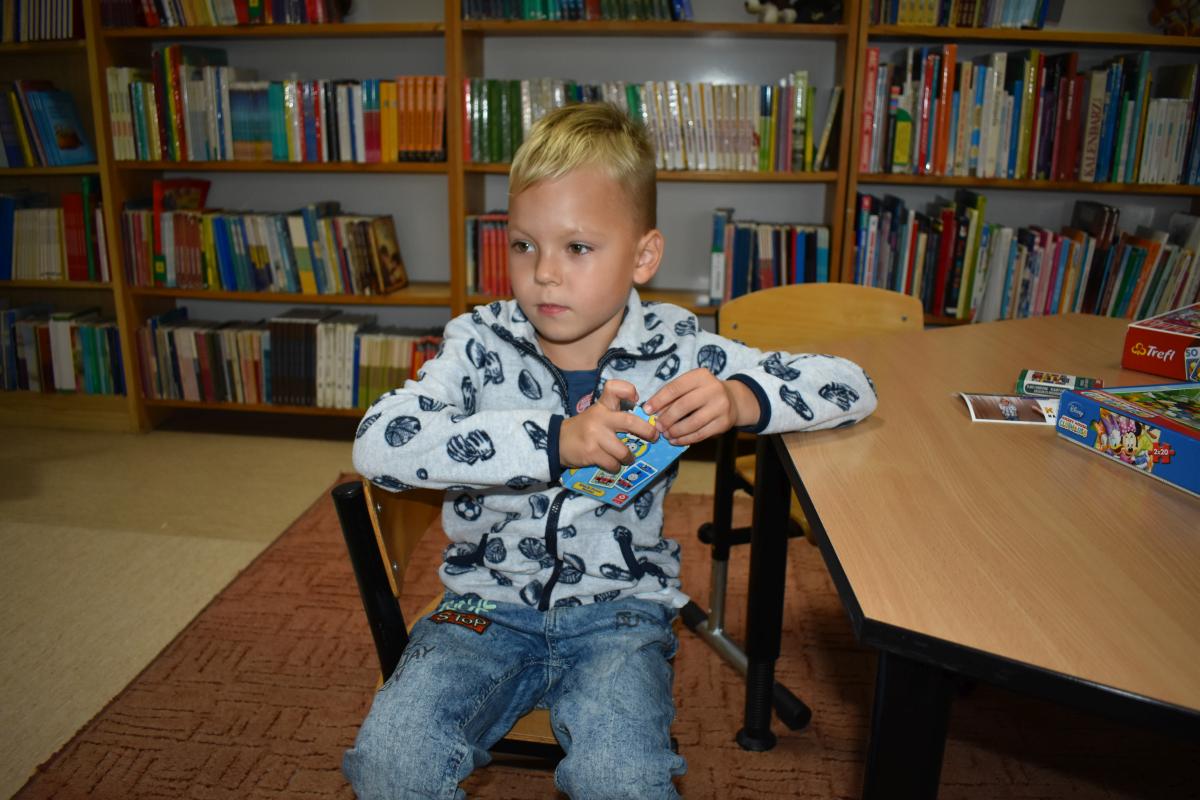 Chłopczyk siedzi przy stoliczku i trzyma w rękach karty do gry 