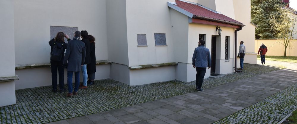 Kilka osób poszukuje ciekawych tablic wbudowanych w ściany kościoła na zewnątrz
