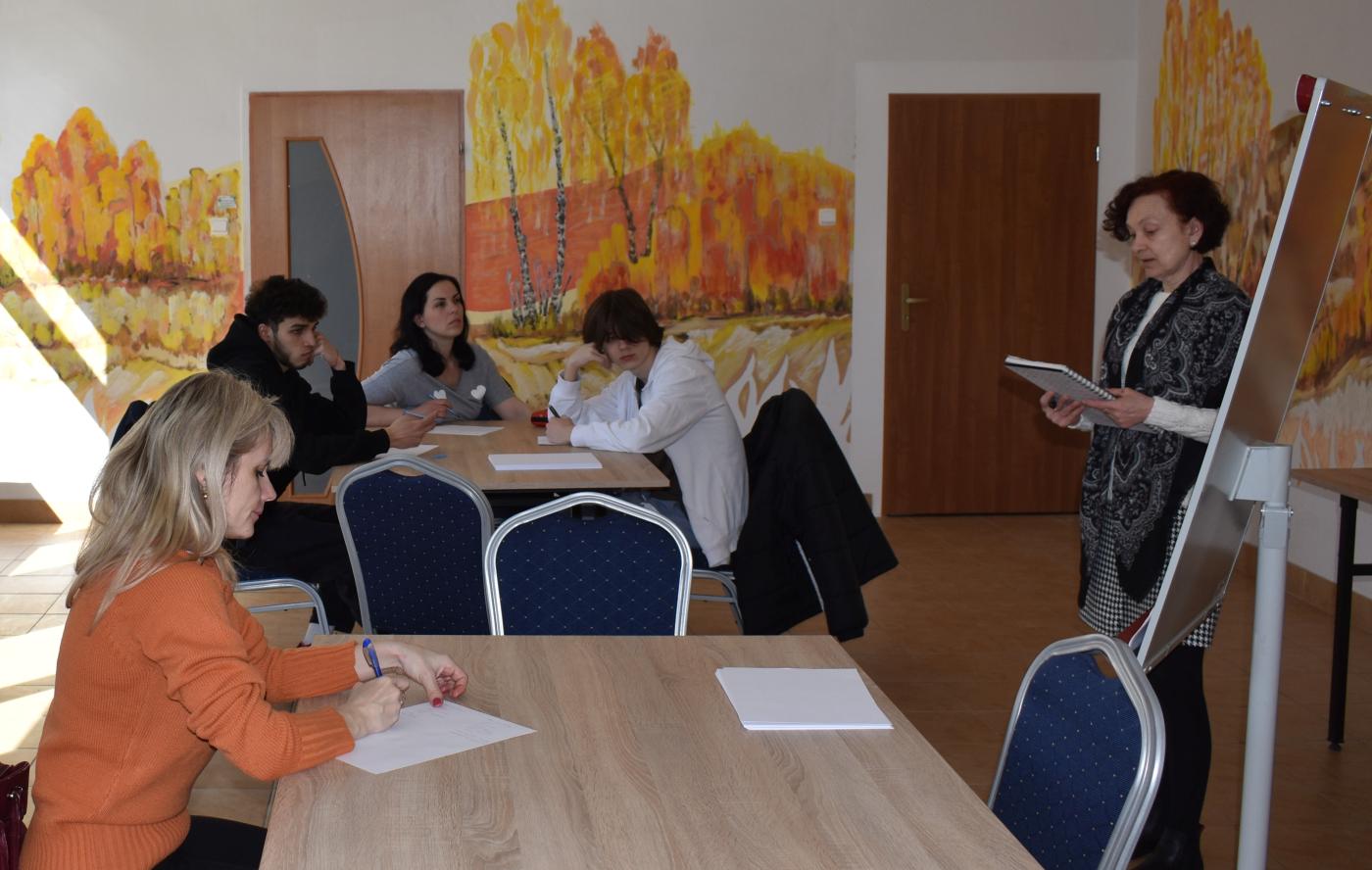 4 osoby siedzą przy dwóch stolikach a Pani czyta