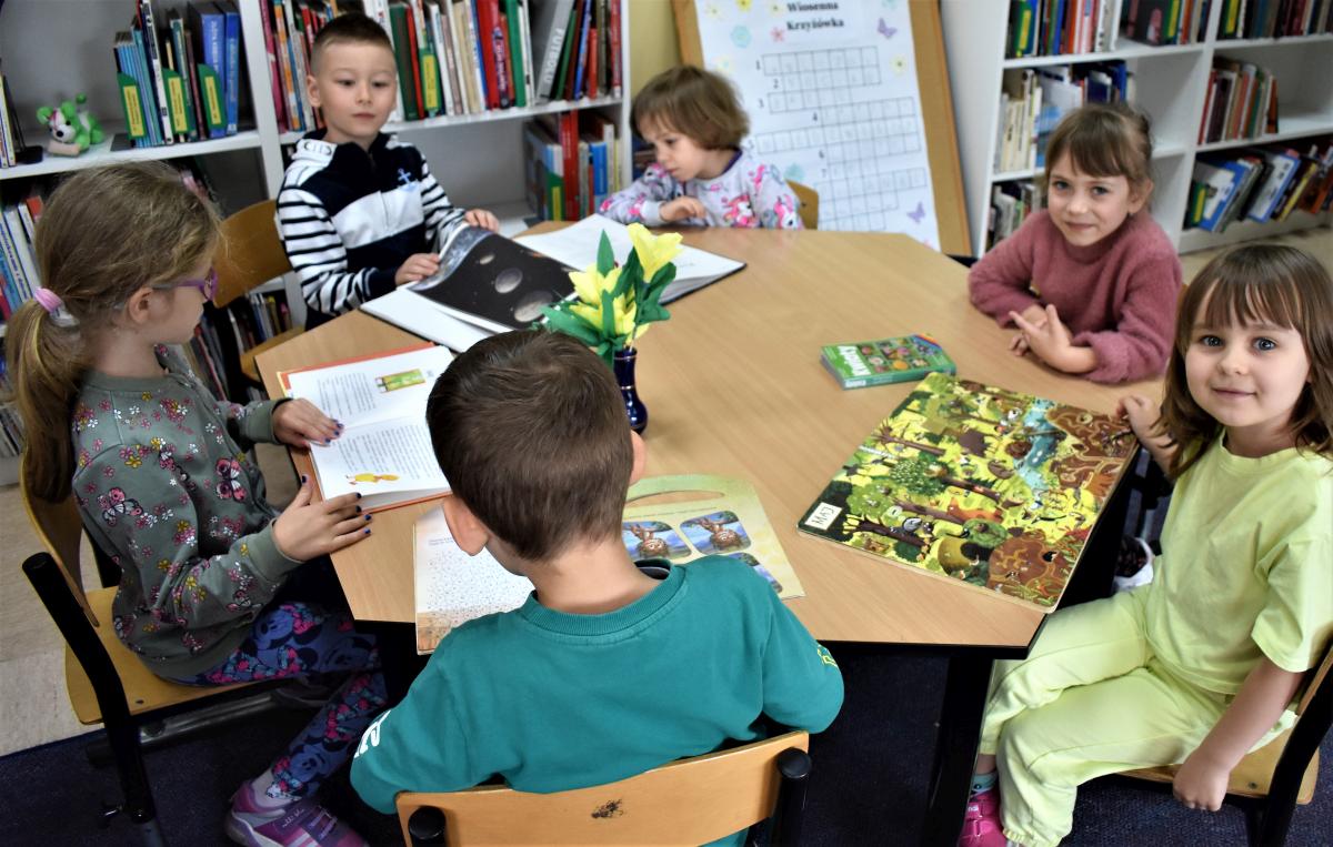 Sześcioro dzieci siedzi przy stoliku i ogląda książki