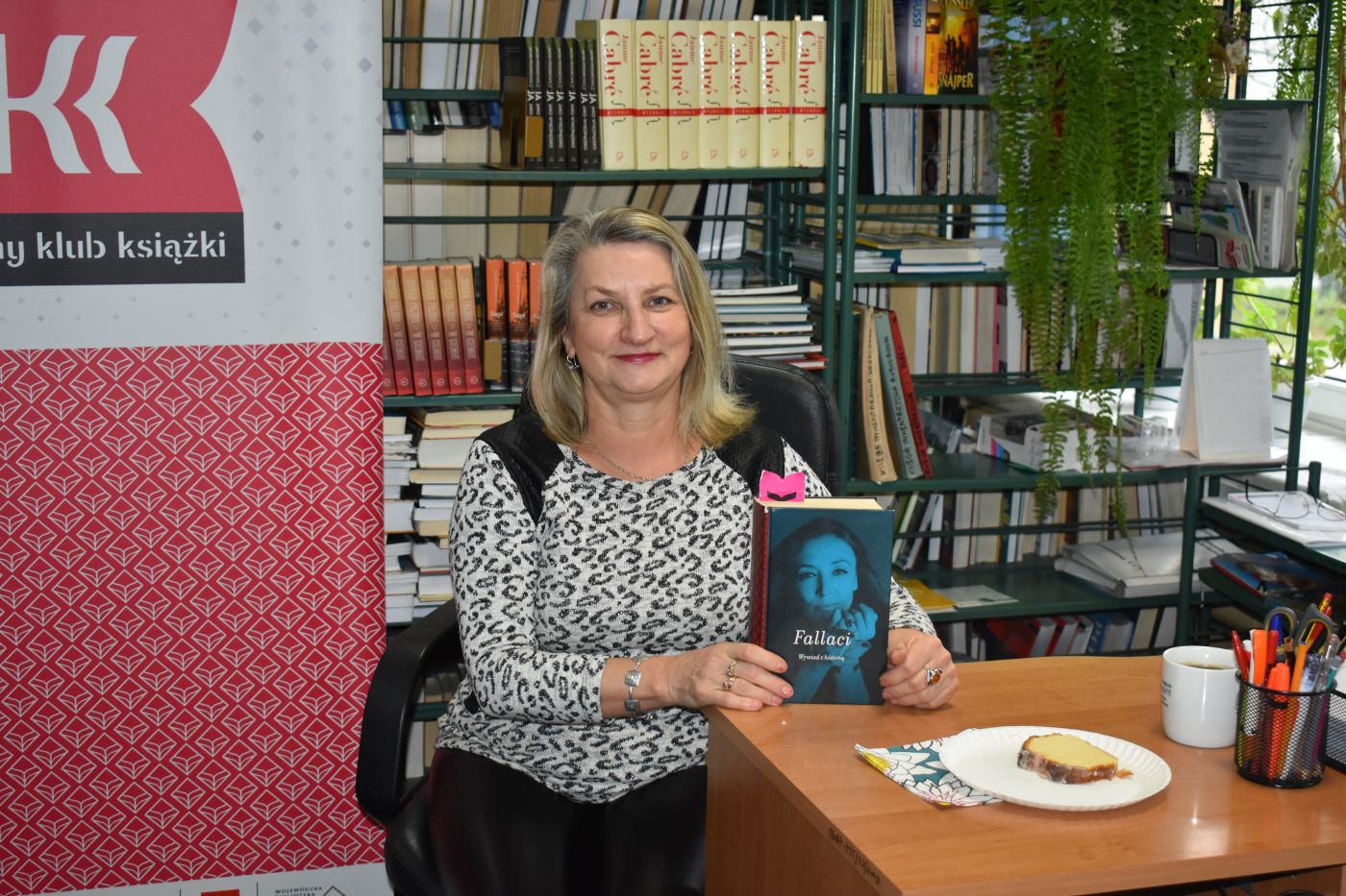 Pani siedzi przy stoliku i prezentuje książkę