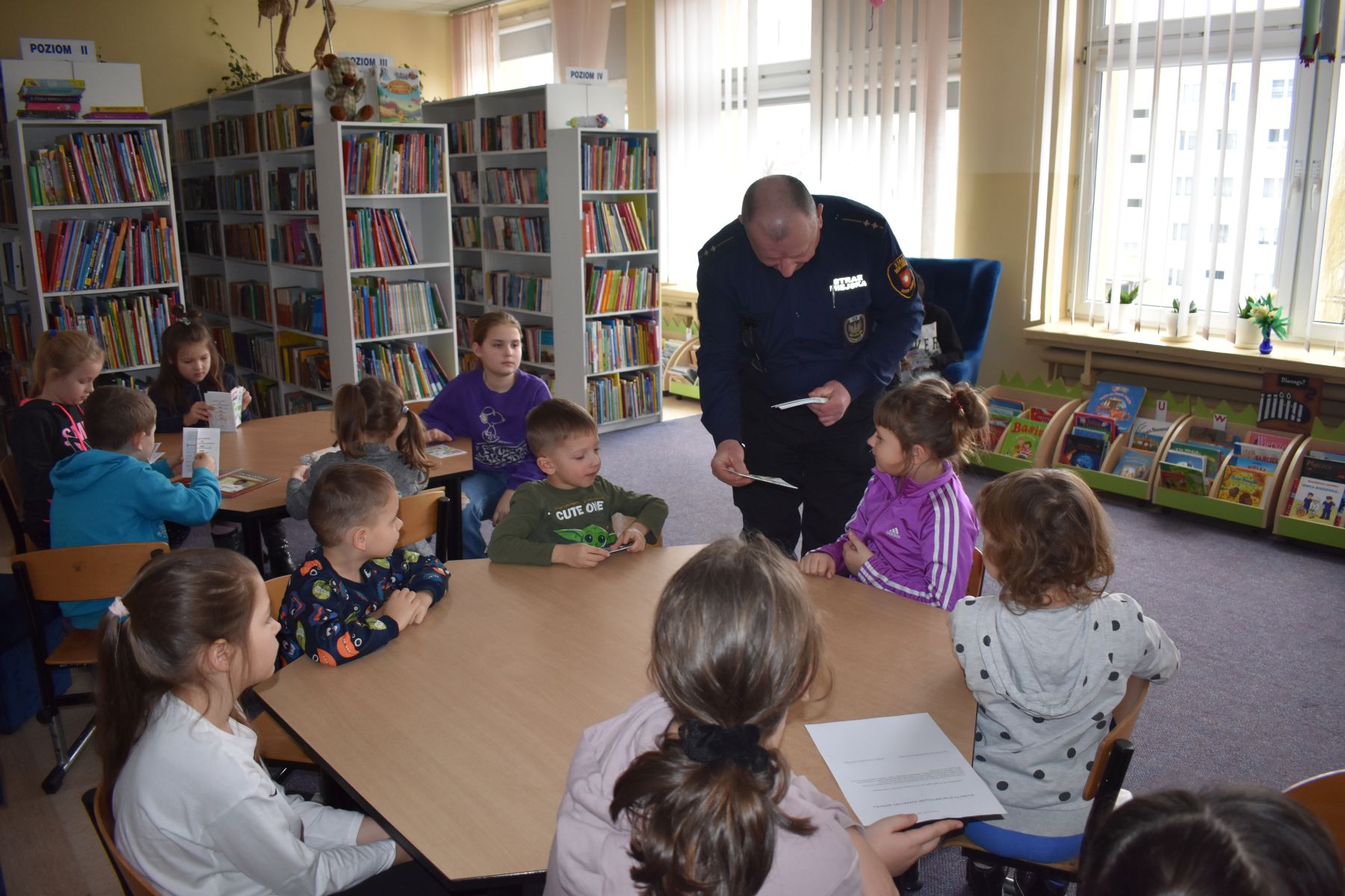 Dzieci otrzymują ulotki informacyjne od funkcjonariusza Straży Miejskiej
