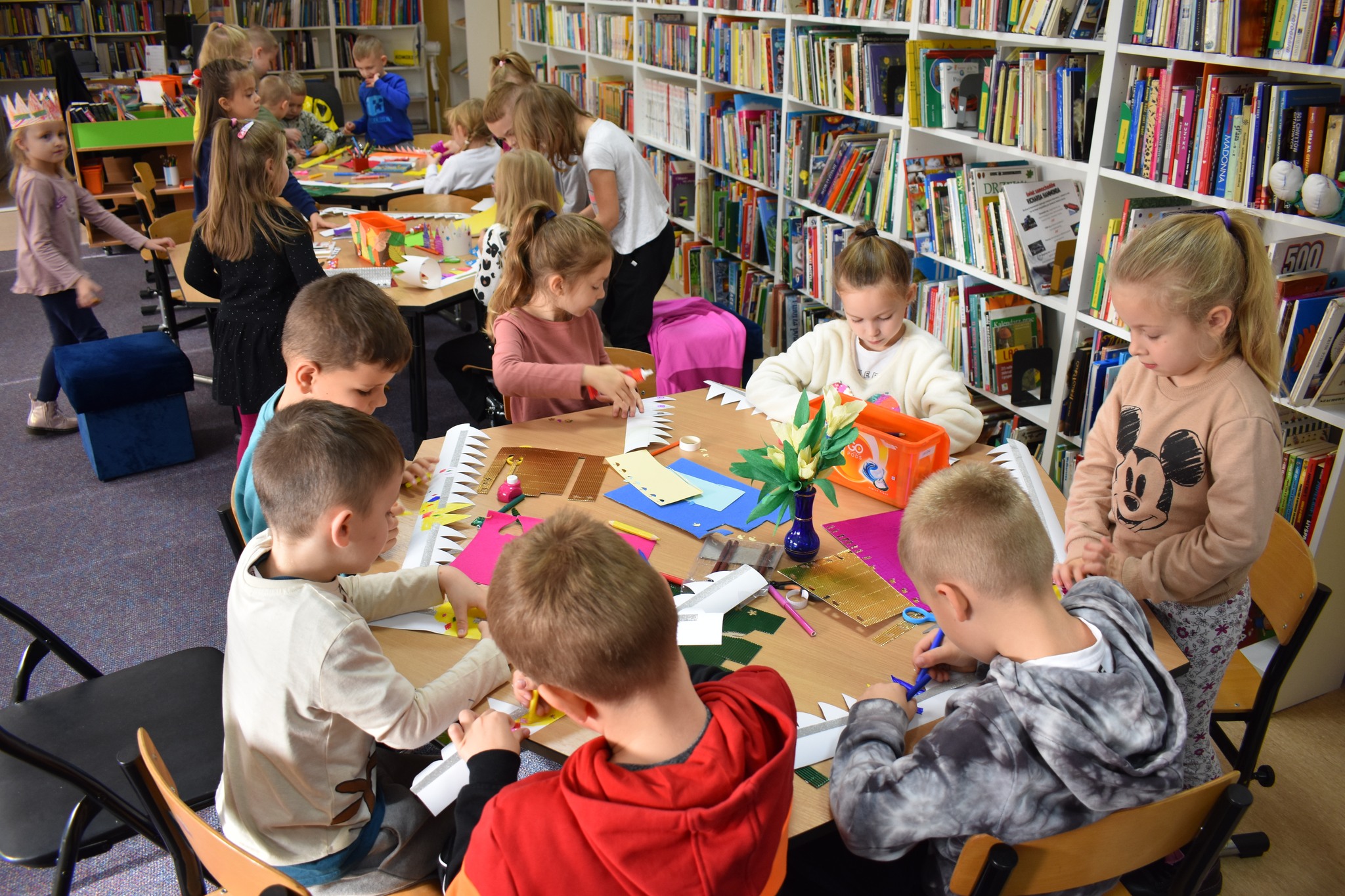 Dzieci siedzą przy stolikach i wykonują prace plastyczne