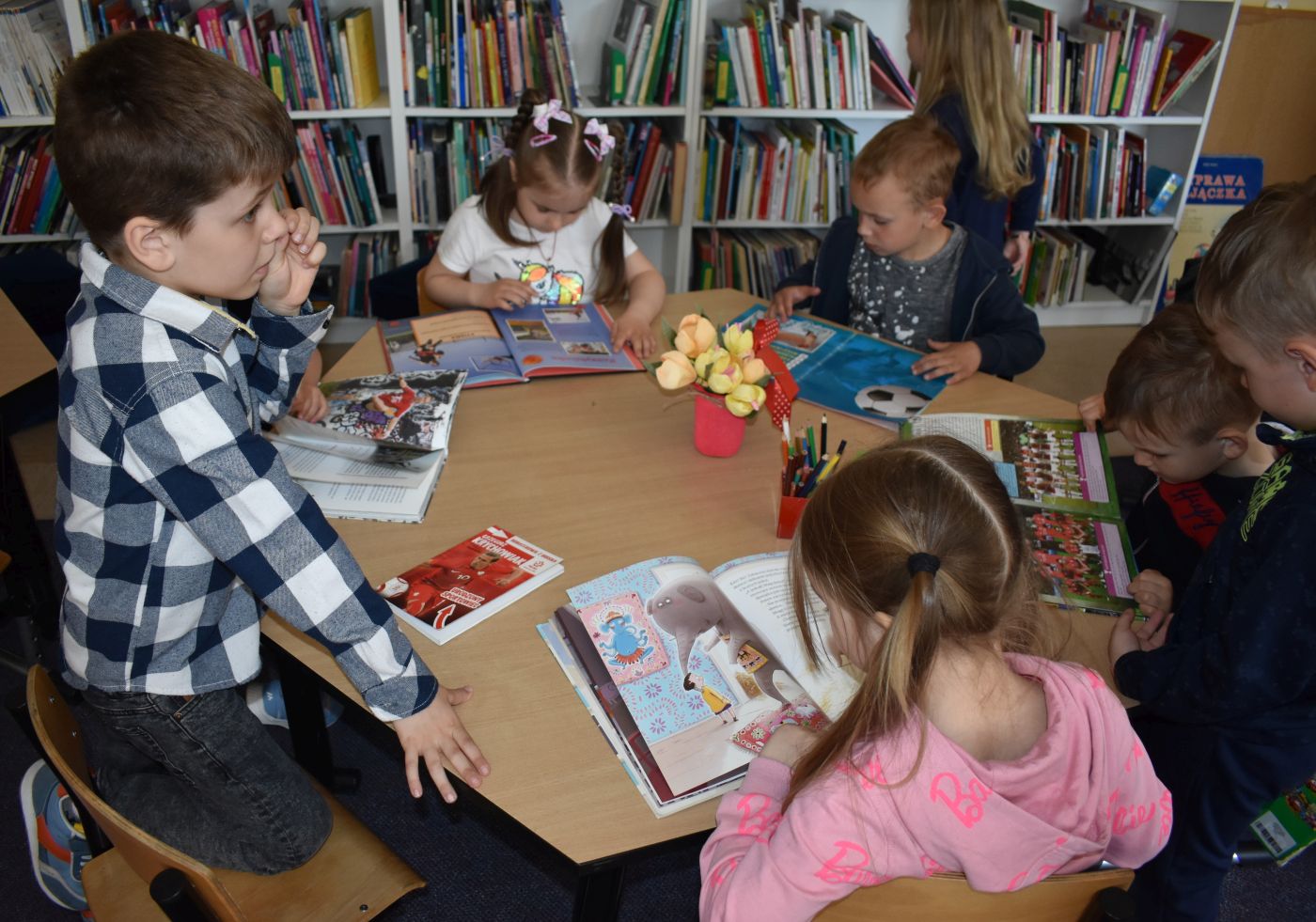 Dzieci siedzą przy stoliku i oglądają książki