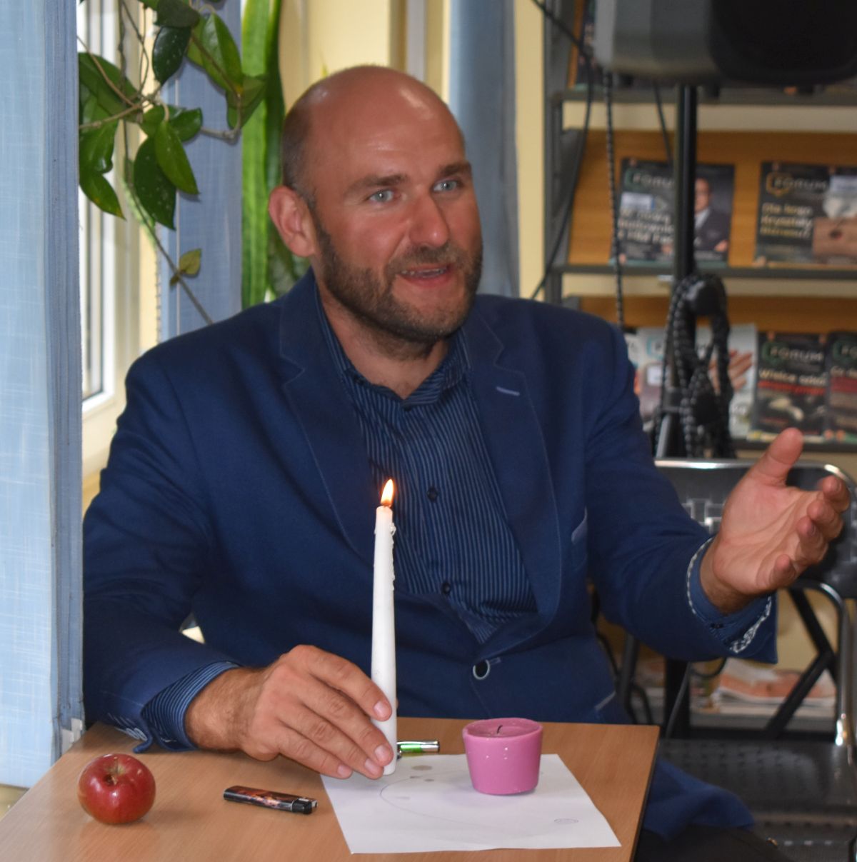 Pan siedzi przy stoliku i trzyma w dłoniach świeczkę
