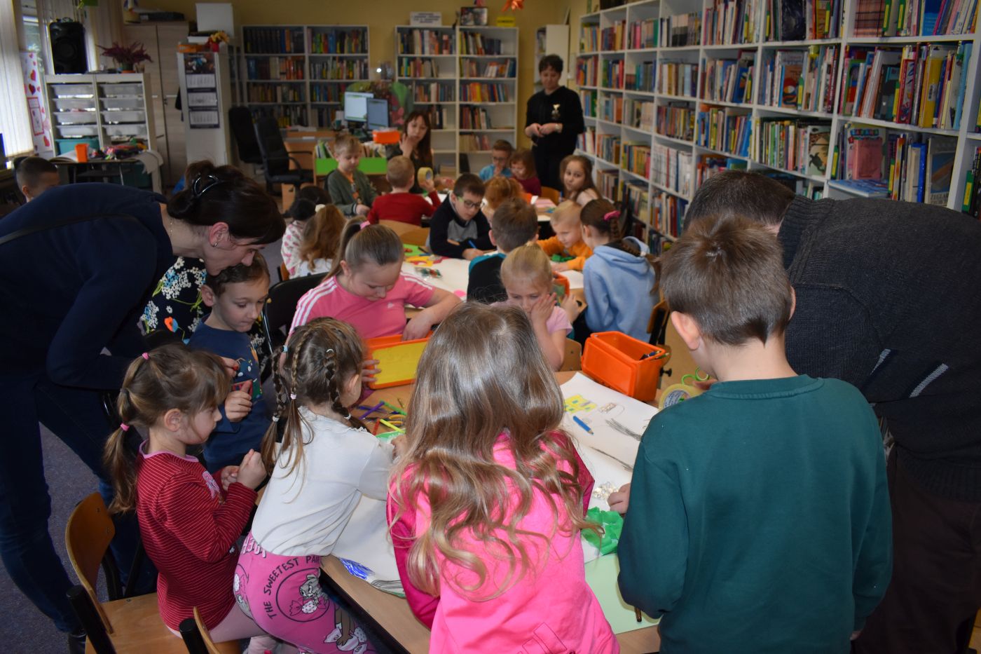 Dzieci siedzą przy trzech stolikach