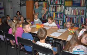 Grupa dzieci siedzi przy stolikach, na których leżą rysunki