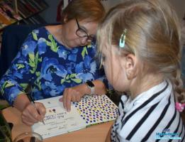 Autorka wpisuje autograf w książkę, przed nią czeka dziewczynka