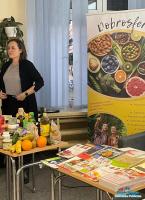 Prelegenta w czasie wykładu, na pierwszym planie książki i produkty spożywcze