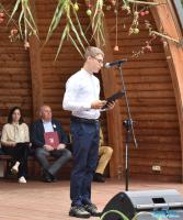 Chłopiec w białej koszuli stoi na scenie i czyta do mikrofonu