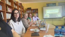 Uśmiechnięte osoby siedzące przy stole. W tle prezentacja o Bibliotece w Rytwianach