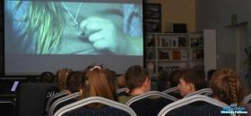 dzieci siedzą na krzesłach a w tle widać slajd z filmu