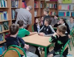 Pan szuka książki na regale a dzieci siedzą przy stolikach Pan szuka książki na regale a dzieci siedzą przy stolikach