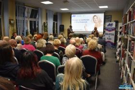 Pan i Pani stoją podczas spotkania a zebrani siedzą na krzesłach