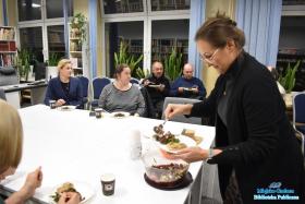 Kobieta nakłada sałatkę na talerz, obok inne osoby spożywające posiłek