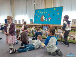 Sześcioro dzieci siedzi na podłodze i oglądają książki a chłopiec z dziewczynką stoją obok