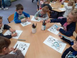 sześcioro dzieci siedzi przy stoliku i koloruje rysunki