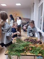 Trzy dziewczynki stoją przy stole na którym leżą szyszki, kasztany oraz liście