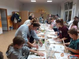 Dzieci i rodzice stoją oraz siedzą pry długim stole i wykonują jesienne ozdoby