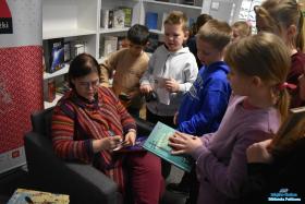 Pani siedzi w fotelu i podpisuje książkę, a obok niej stoją dzieci