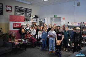 Pani siedzi w fotelu, obok niej do zdjęcia grupowego pozują dzieci