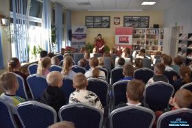 Pani stoi i mówi do dzieci, które siedzą na krzesłach