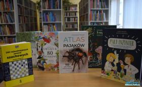 Sześć książek stoi na stoliku, a w tle widać regały z książkami