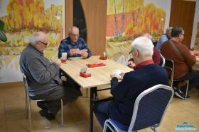 Czterech Panów siedzi przy stoliku i trzyma w dłoniach karty