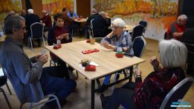 Trzy Panie i Pan siedzą przy stoliku a w tle widać innych grających