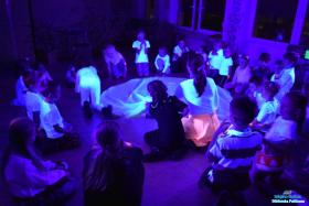 Pani z dziewczynką wyjmują coś spod chusty, a dzieci siedzą obok