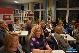 Duzo osób siedzi przy białych stolikach popijając kawę