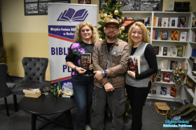 Dwie uśmiechnięte paie trzymają książki i pozują razem z panem w czapce