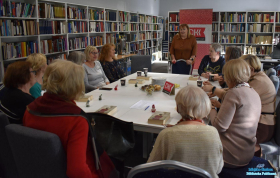 Panie siedzą przy stoliku a jedna Pani stoi