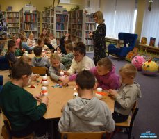 Pani stoi obok stolików, a dzieci wykonują prace plastyczne
