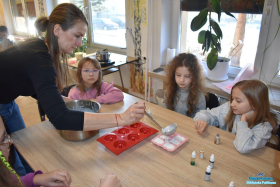 Pani nalewa płynna masę do foremek, a dziewczynki siedzą przy stoliku