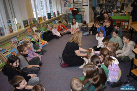 Dzieci siedzą w kółku, a Pani siedzi z pieskiem, który bawi się z dziećmi