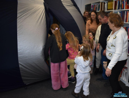 Dzieci wchodzą do namiotu, a dorośli stoją obok regałów z książkami