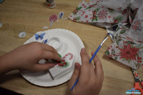 Dziecko nakleja naklejki na formę i trzyma w dłoni pędzelek