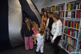 Dzieci wchodzą do namiotu, a dorośli stoją obok regałów z książkami