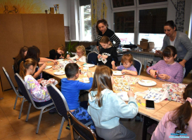 Dzieci wykonują prace plastyczne, a dwie Panie stoją obok stołu