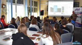 Pan stoi oraz prowadzi prelekcję, młodzież siedzi na krzesłach