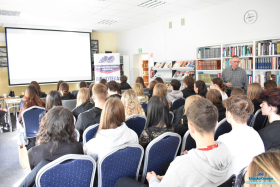 Pan stoi obok młodzieży, która siedzi na krzesłach