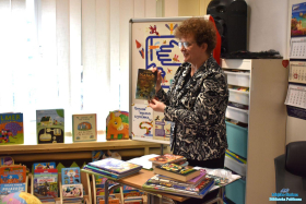 Pani trzyma w dłoniach książkę, a przed nią na stoliku leżą książki