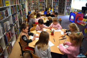 Dzieci siedzą przy stolikach i wykonują prace plastyczne