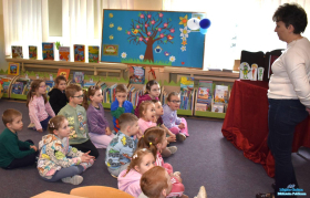 Pani stoi  a dzieci siedzą na dywanie