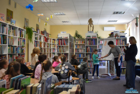 Dwie Panie i dziewczynka stoją przy tablicy, a dzieci siedzą