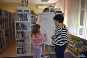 Pani stoi obok dziewczynki, która wpisuje hasło do krzyżówki